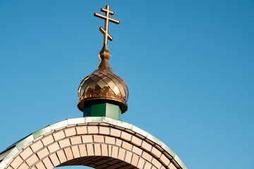 Fototapeta na wymiar cross on the dome of the Orthodox Church in Russia against the blue sky and a semicircular arch on which the dome is installed