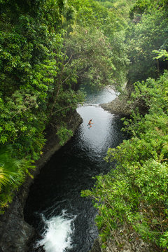 A brave man jumping from a cliff into a tropical river