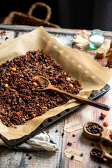 homemade baked chocolate granola with nuts, oat flakes on baking tray with parchment stands on grey wooden table