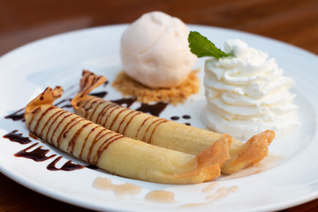 Deep fried bananas or sweet banana fritters with vanilla ice cream, whip cream and chocolate syrup sauce on top. Delicious Thai dessert menu in restaurant.
