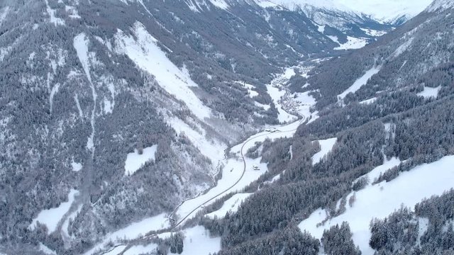 4K Mountain valley road in winter cinematic aerial shot. Camera tilting up to discover the frozen mountain panorama