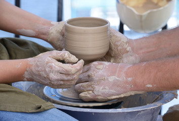 Teaching of wheel throwing. Potter’s hand correcting woman’s ones during shaping clay blank on a potter's wheel