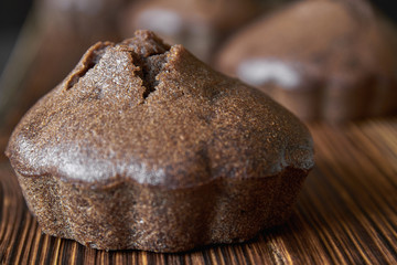 Homemade coffee muffin on a wooden board with a group of chocolate cupcakes on dark wooden background. Closeup, selective focus