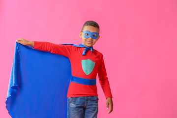 Cute African-American boy dressed as superhero on color background