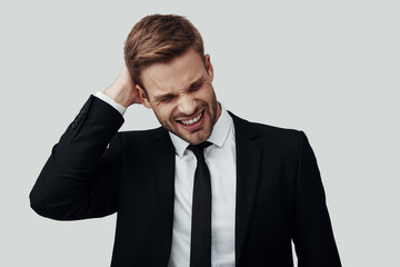 Frustrated young man in formalwear making a face while standing against grey background