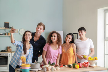 Happy friends taking selfie while cooking together in kitchen