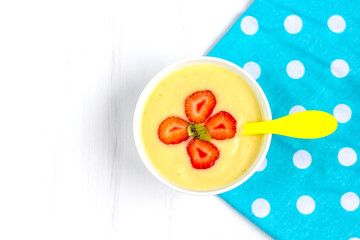 Healthy breakfast porridge for kids. Bowl of baby food on a fabric on white wooden background. The concept of proper nutrition and healthy food.