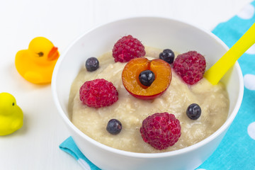 Healthy breakfast porridge for kids. Bowl of baby food on a fabric on white wooden background.