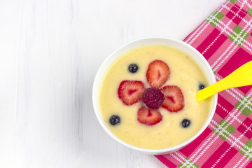 Healthy breakfast porridge for kids. Bowl of baby food on a fabric on white wooden background. The concept of proper nutrition and healthy food.