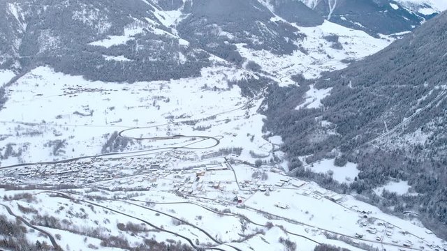 Winter season frozen mountain landscape and village in the valley. Camera tilting up to discover the white mountains on a cloudy day