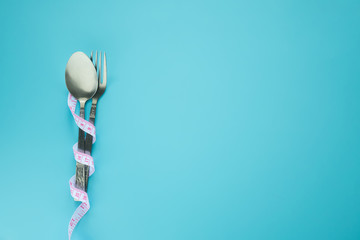 spoon and fork wrapped in measuring tape isolated on blue background with copy space. diet , food...