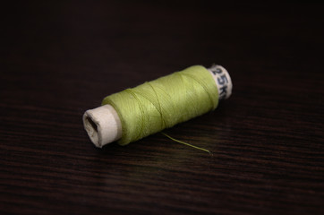 Spool of green sewing thread on dark wooden table background