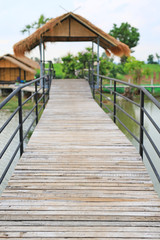 Wooden bridge crossing river to countryside pavilion in Thailand.