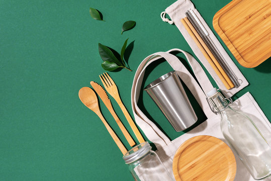 Sustainable lifestyle. Zero waste, plastic free shopping concept. Cotton bags, glass jar, bottle, metal cup, straws for drinking, bamboo cutlery and boxes on green background.
