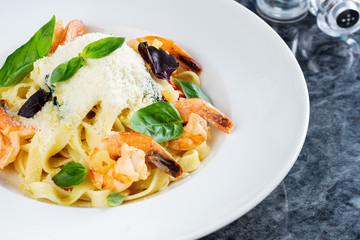 Top view pasta with seafood, shrimp, basil, and parmesan on marble table. Spaghetti in a white bowl. Traditional Italian cuisine. Copy space. Selective focus. Food photography