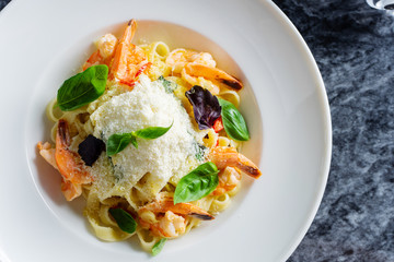Top view pasta with seafood, shrimp, basil, and parmesan on marble table. Spaghetti in a white bowl. Traditional Italian cuisine. Copy space. Selective focus. Food photography