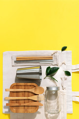 Sustainable lifestyle. Zero waste, plastic free shopping concept. Cotton bags, glass jar, bottle, metal cup, straws for drinking, bamboo cutlery and boxes on yellow background.