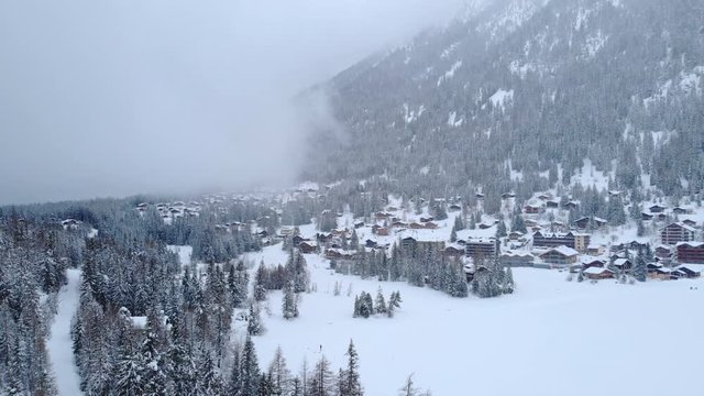 4K Mountain village on a cold winter day aerial shot. Clouds and fresh snow in late afternoon