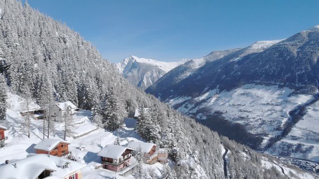 4K Winter in Switzerland cinematic aerial shot. Camera flying over chalets with scenic valley in the background