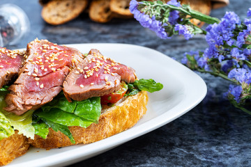 Close up view on delicious italian bruschetta with roast beef, lettuce, cherry tomato and sauce. Italian cuisine. Selective focus on sandwich with meat on marble table. Copy space