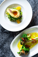 Top view on tasty and luxury food with restaurant food styling on marble table. Fresh and grilled vegetables salads with avocado, broccoli in white plate. Food photography background