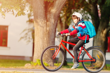Fototapeta na wymiar Child with rucksack riding on bike in the park near school