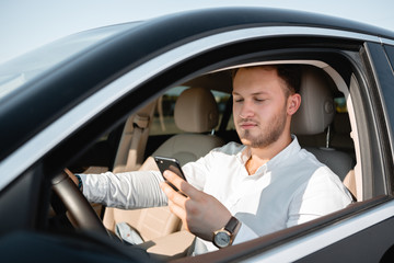 Young businessman smiling looking at mobile phone while driving a car.
