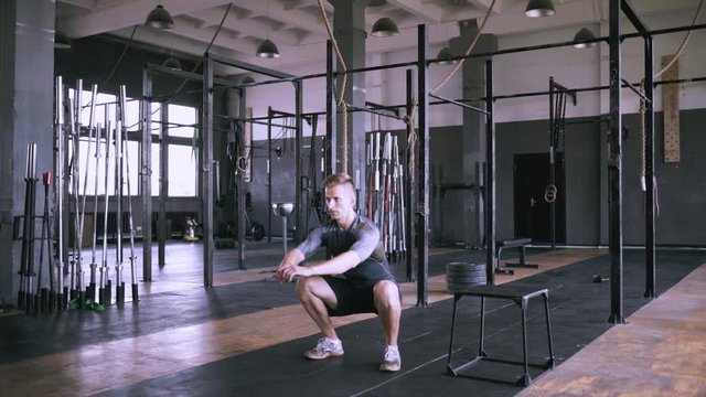 Man squats at gym. Effective powerlifting squatting. Male fitness instructor showing squat exercise at modern plase. Muscular man doing slight crouch, strength training exercise.