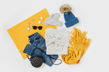 Blue winter hat with jeans, sweater, handbag and yellow scarf on white background. Women's stylish autumn or winter outfit. Trendy clothes collage. Flat lay, top view.