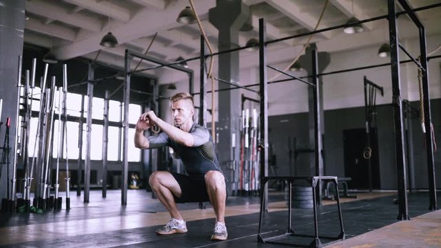 Man squats at gym. Effective powerlifting squatting. Male fitness instructor showing squat exercise at modern plase. Muscular man doing slight crouch, strength training exercise