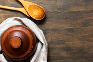 Top view of clay pot and wooden spoons on wooden background with copy space
