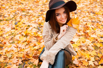 Carefree young woman in trendy vintage hat sitting in park and laughing. Curly cute girl in good...