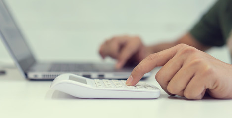 close up on man hand pressing calculator for counting about monthly expenses with using laptop for checking list at home for millennial lifestyle concept