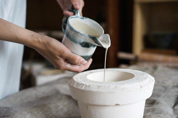 Female hands pour pottery mixture into a mold. Shaped method for making clay dishes. Handwork....