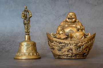 Figurine Cheerful Hotei  and golden bell close-up, soothing and meditative. Smiling Buddha and golden bell Isolated on gray background. Symbols of Asia