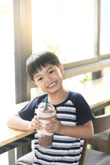 An Asian boy drinking a plastic glass of cold chocolate. 
