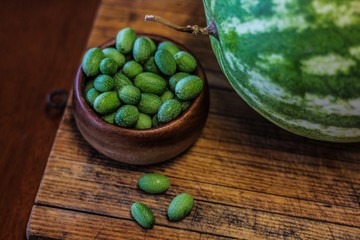 Still Life of a Large Watermelon on a Wooden Board next to a small wooden bowl of Mexican Sour Gherkins, selective focus on foreground