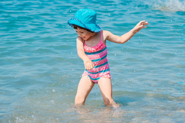 little girl in a swimsuit splashing her legs in the sea