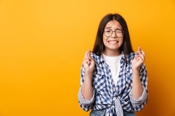 Nervous emotional young cute teenage girl in glasses posing isolated over yellow wall background showing hopeful please gesture.