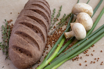composition of dark bread with scattered buckwheat, sprigs of rosemary, fresh mushrooms and green onions on baking canvas