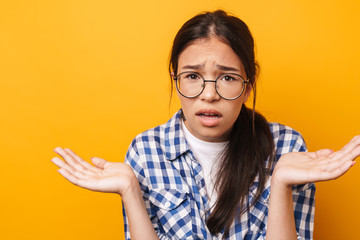 Confused teenage girl in glasses posing isolated over yellow wall background.