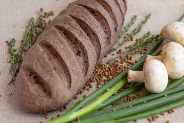 composition of dark bread with scattered buckwheat, sprigs of rosemary, fresh mushrooms and green onions on baking canvas