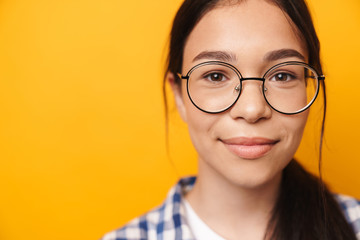 Positive optimistic happy young cute teenage girl in glasses posing isolated over yellow wall background.