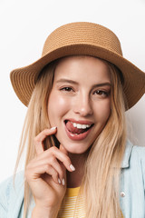 Flirty amazing young pretty woman wearing hat posing isolated over white wall background showing tongue.