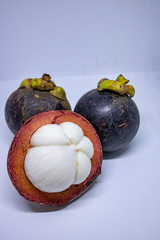 Group of  mangosteen fruits cut open in half showing the white flesh and a rim pink color of the shell against white background