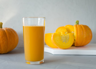 Fresh pumpkin juice in a glass glass, two pumpkins in the background on a gray background. The concept of proper, healthy eating. Autumn harvest. Horizontal orientation, copy space.