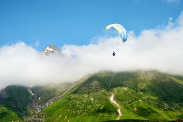beautiful view of green mountains and melting glaciers with a flying paraglider in the sky of sunny Georgia (country)