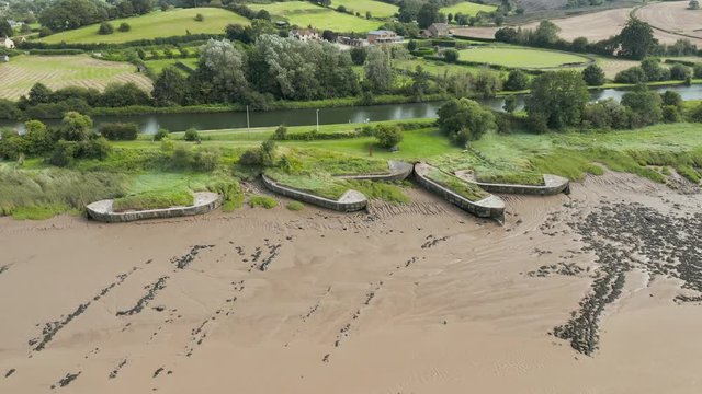 Aerial drone flight along abandoned shipwreck hulks on the side of a muddy river (Purton Hulks, England)