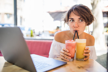 Lifestyle fashion portrait of young pretty girl drinking milkshake in cafe outdoors.