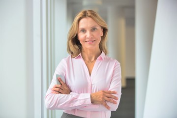 Portrait of confident businesswoman standing with arms crossed in corridor at office